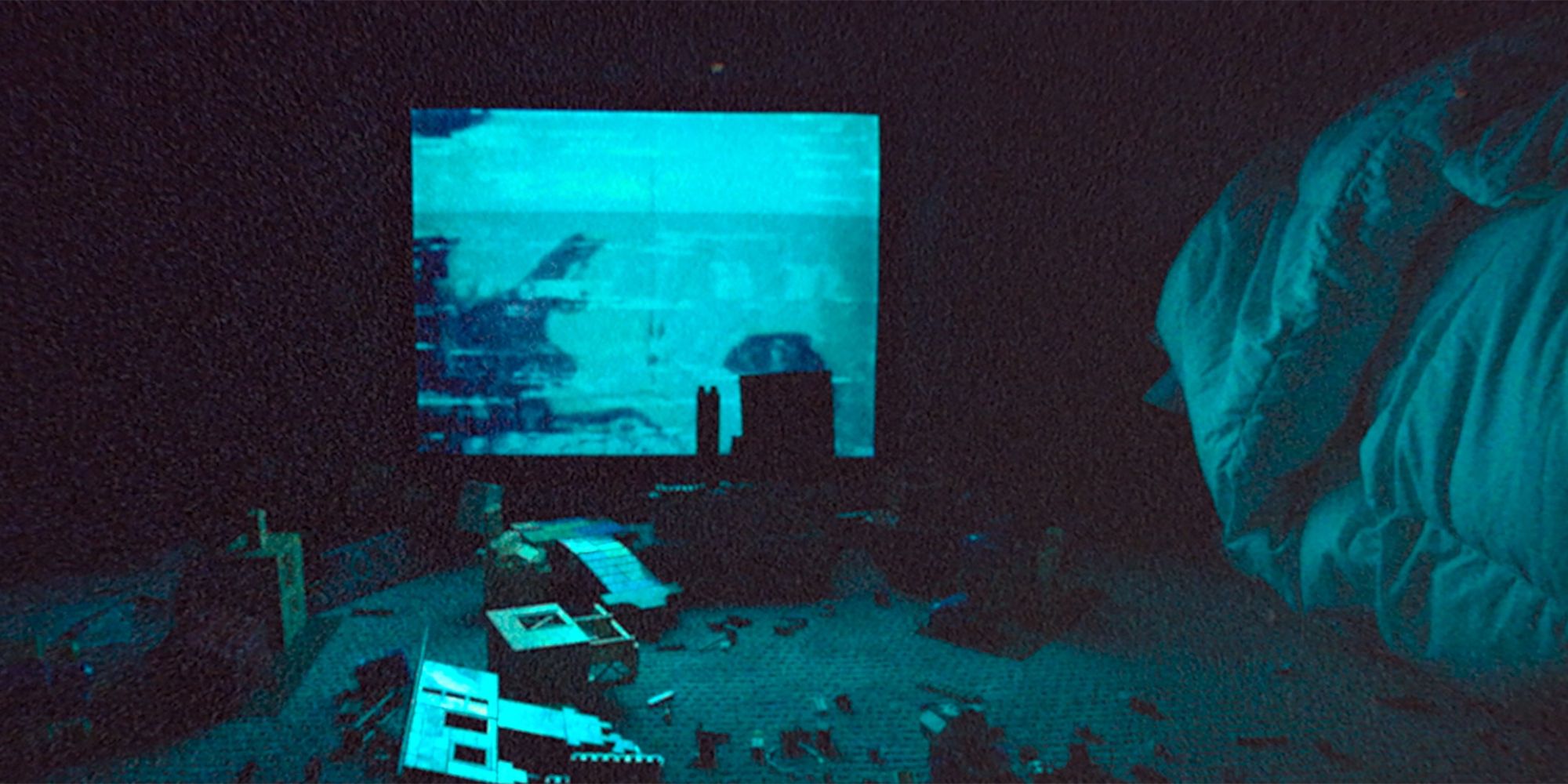 A blue bedroom scene with a comforter on the right and toy wreckage on the ground in Skinamarink