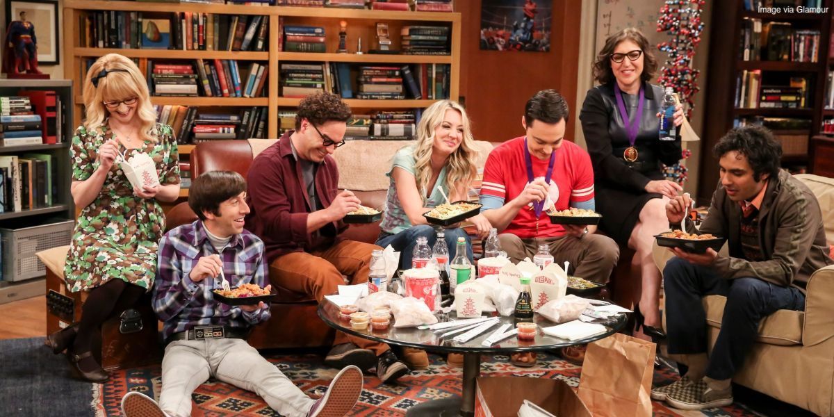 The friends from The Big Bang Theory sitting around the couch eating Chinese take-out and laughing.