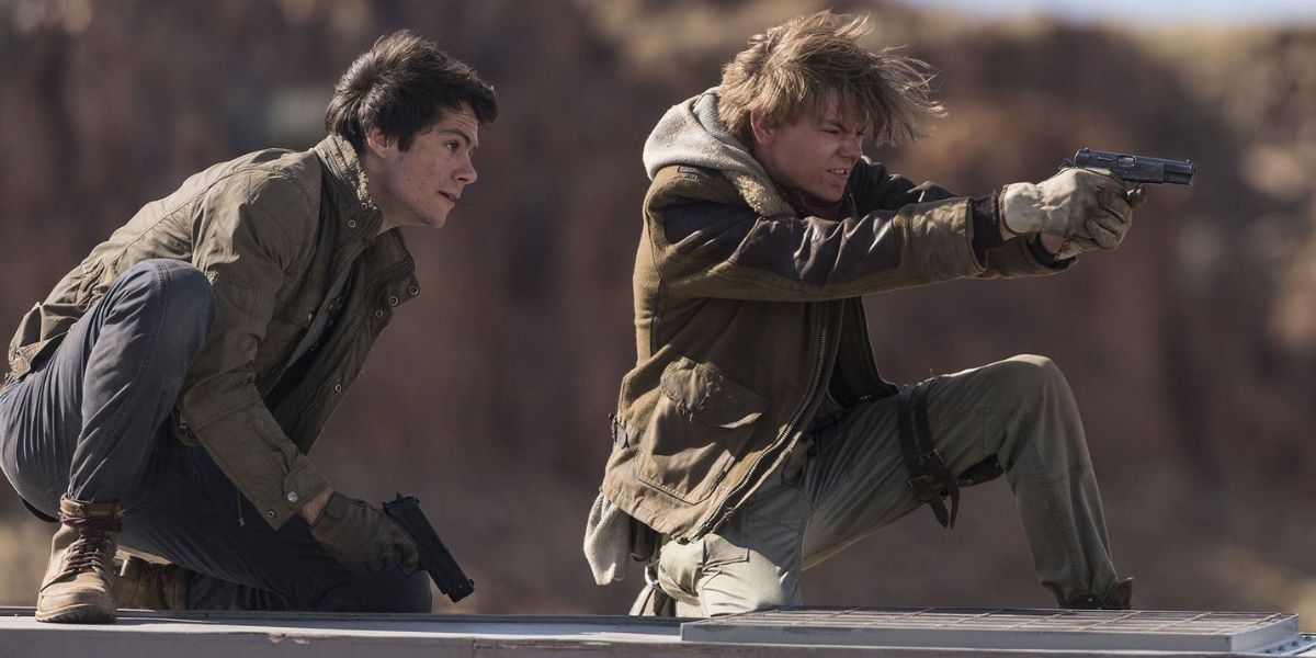 Newt, interpretado por Thomas Brodie Sangster, aponta sua arma enquanto Thomas, interpretado por Dylan O'Brien, olha para trás em The Maze Runner: The Death Cure. 