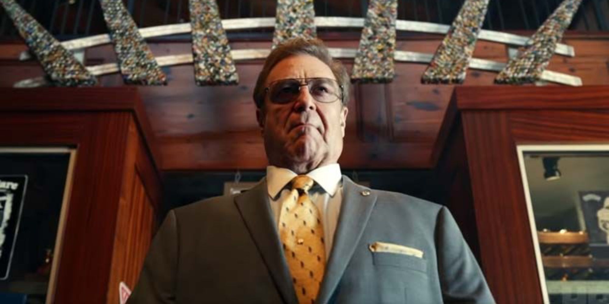 A low down angle view of John Goodman in The Righteous Gemstones, wearing a suit and glasses.