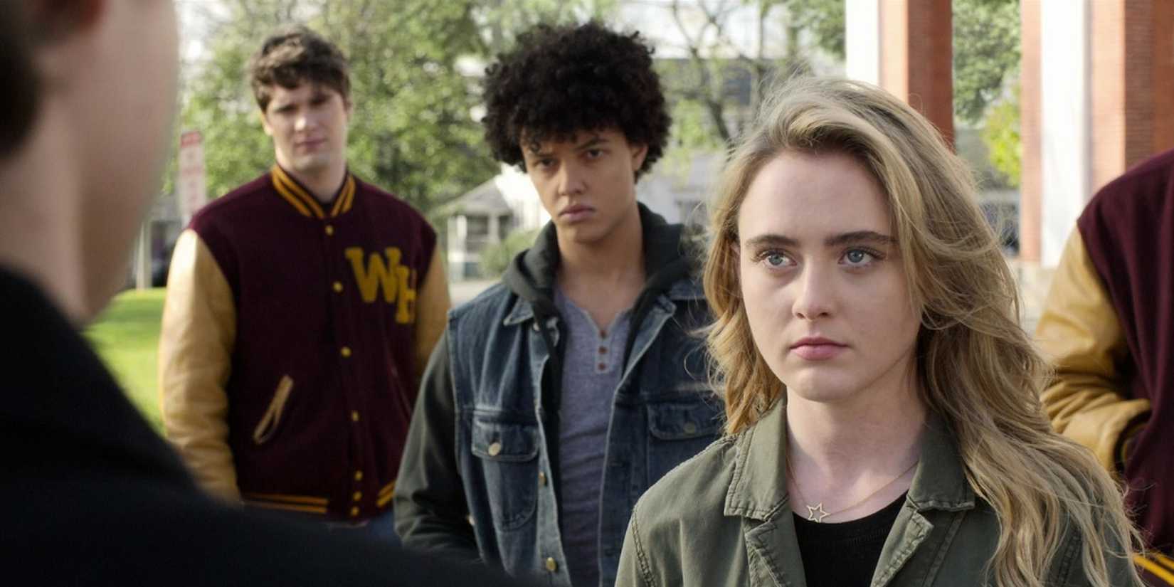 Allie looking at a boy with his back to the camera while two other boys stand behind her in The Society.