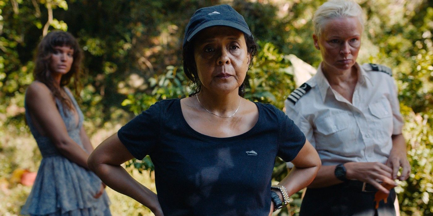 Charlbi Dean Kriek, Dolly De Leon, and Vicki Berlin standing together in a forest in Triangle of Sadness