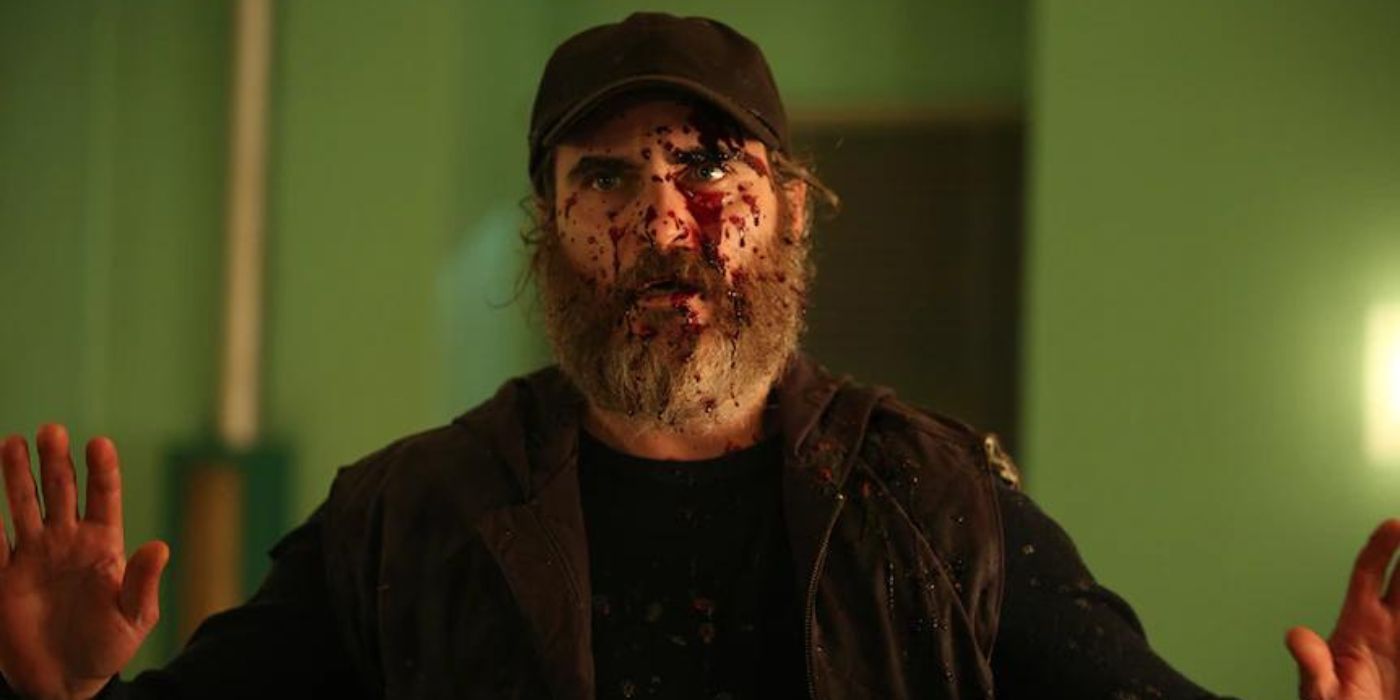 Joaquin Phoenix as Joe with blood splattered on his face and his hands up in surrender in 'You Were Never Really Here.'