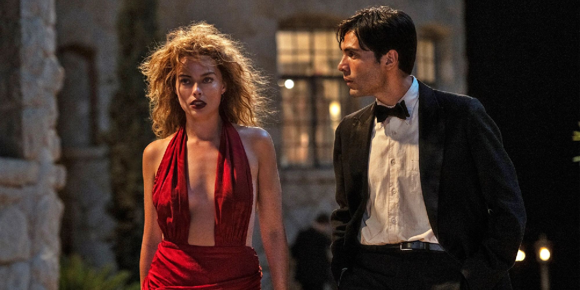 Margot Robbie e Diego Calva como Nellie LaRoy e Manny Torres em trajes elegantes caminhando ao lado de uma mansão