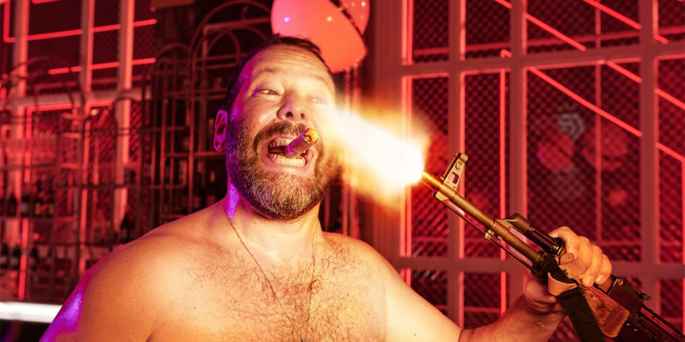 Bert Kreischer allumant un cigare avec un fusil d'assaut dans The Machine 