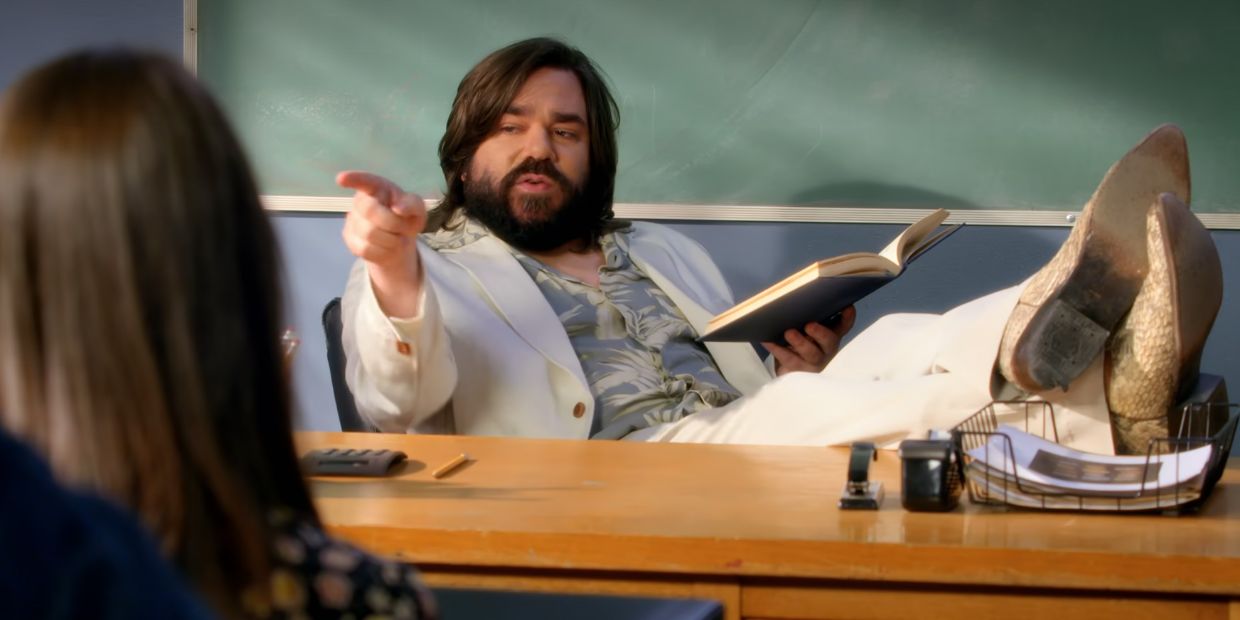 Matt Berry En Tant Que Professeur Desalvo De Community Avec Ses Pieds Sur Un Bureau Tenant Un Livre Et Pointant Du Doigt.