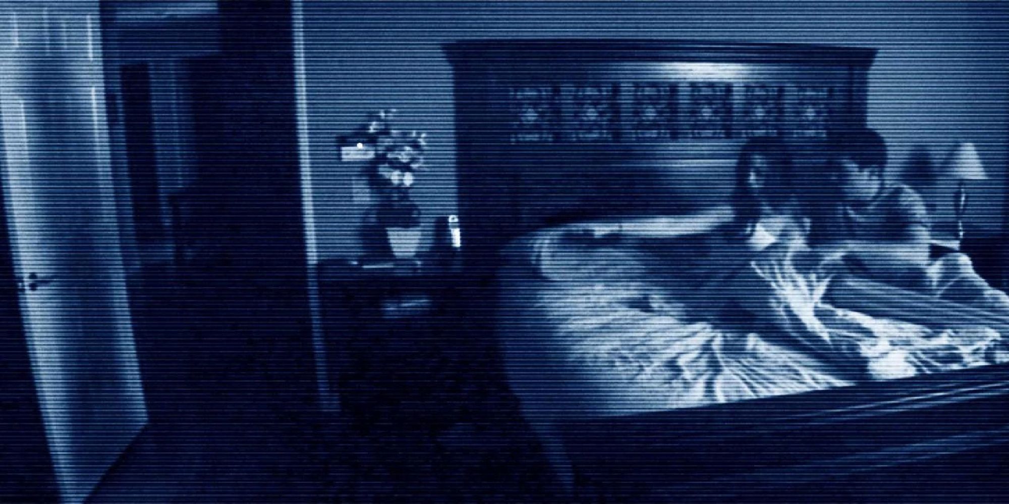 Footage of a woman and her husband sitting in bed in the middle of the night pointing a finger at the door in 'Paranormal Activity'
