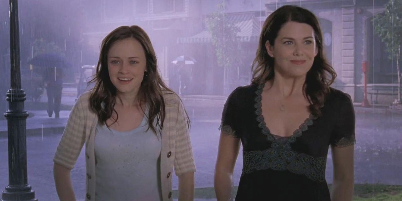 Alexis Bledel as Rory and Lauren Graham as Lorelai smiling in the rain, surprised at the celebration the town has thrown for Rory in the finale of Gilmore Girls