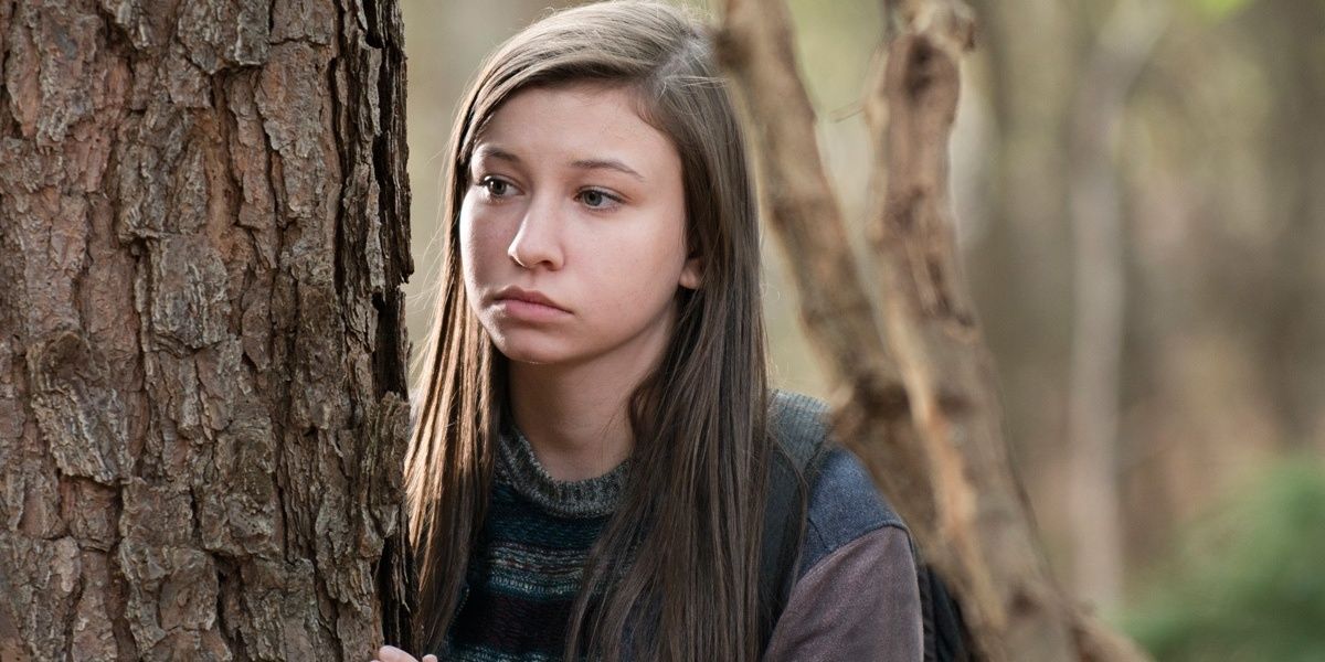 A young survivor peers from behind a tree in the woods in 'The Walking Dead'