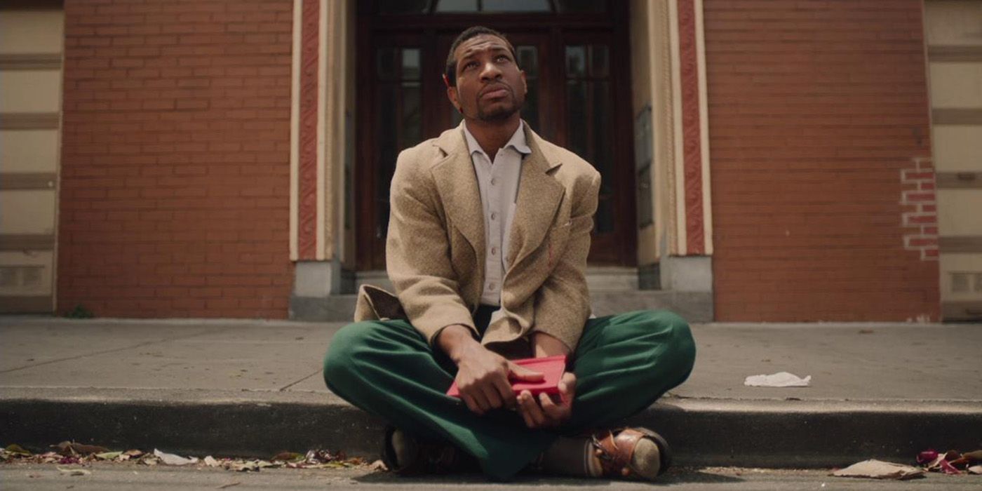 Jonathan Majors sitting on the curb in front of a brick building in The Last Black Man in San Francisco