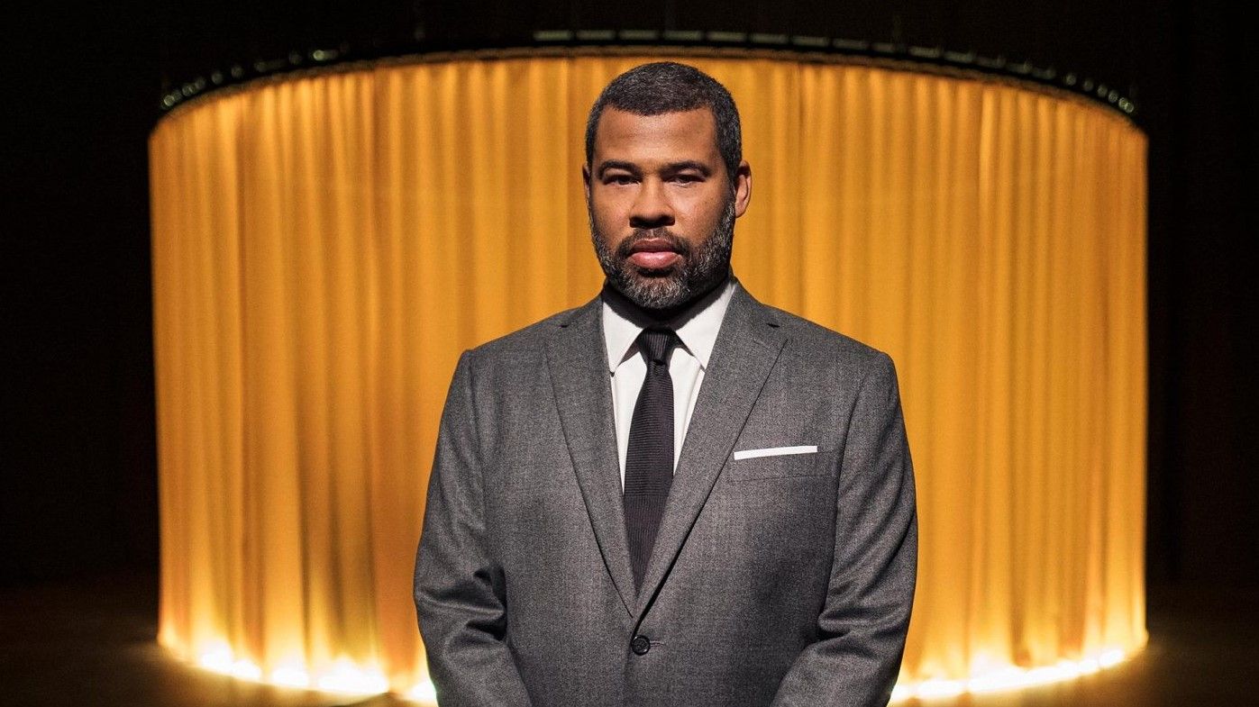 Jordan Peele wearing a grey suit and tie while hosting an episode of The Twilight Zone.