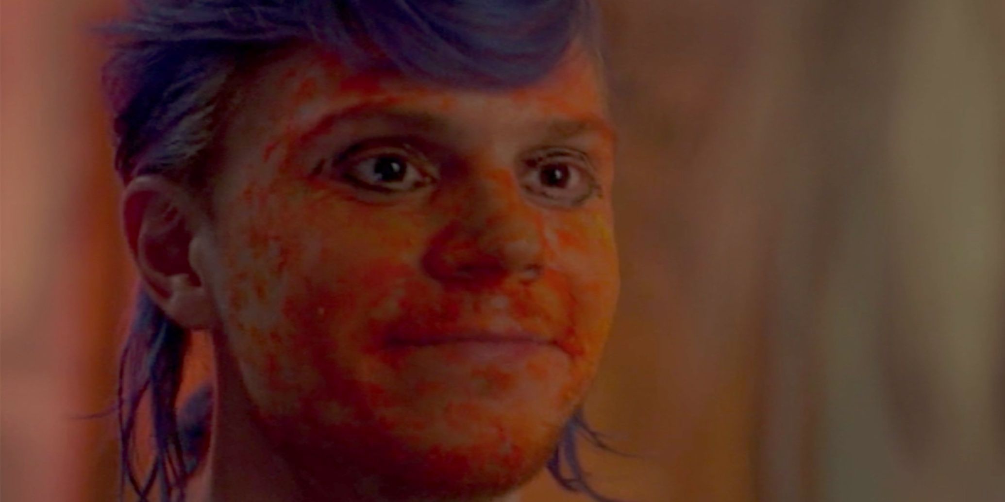 Evan Peters as Kai in 'American Horror Story: Cult.'  He has blue hair and Cheeto dust on his face, and looks to the right with a smile.