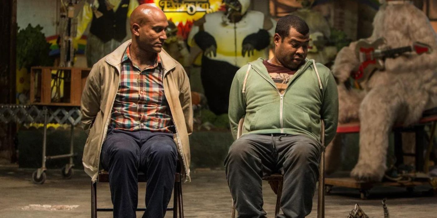 Keegan-Michael Key as Clarence and Jordan Peele as Rell tied up in chairs looking down at the cat in Keanu