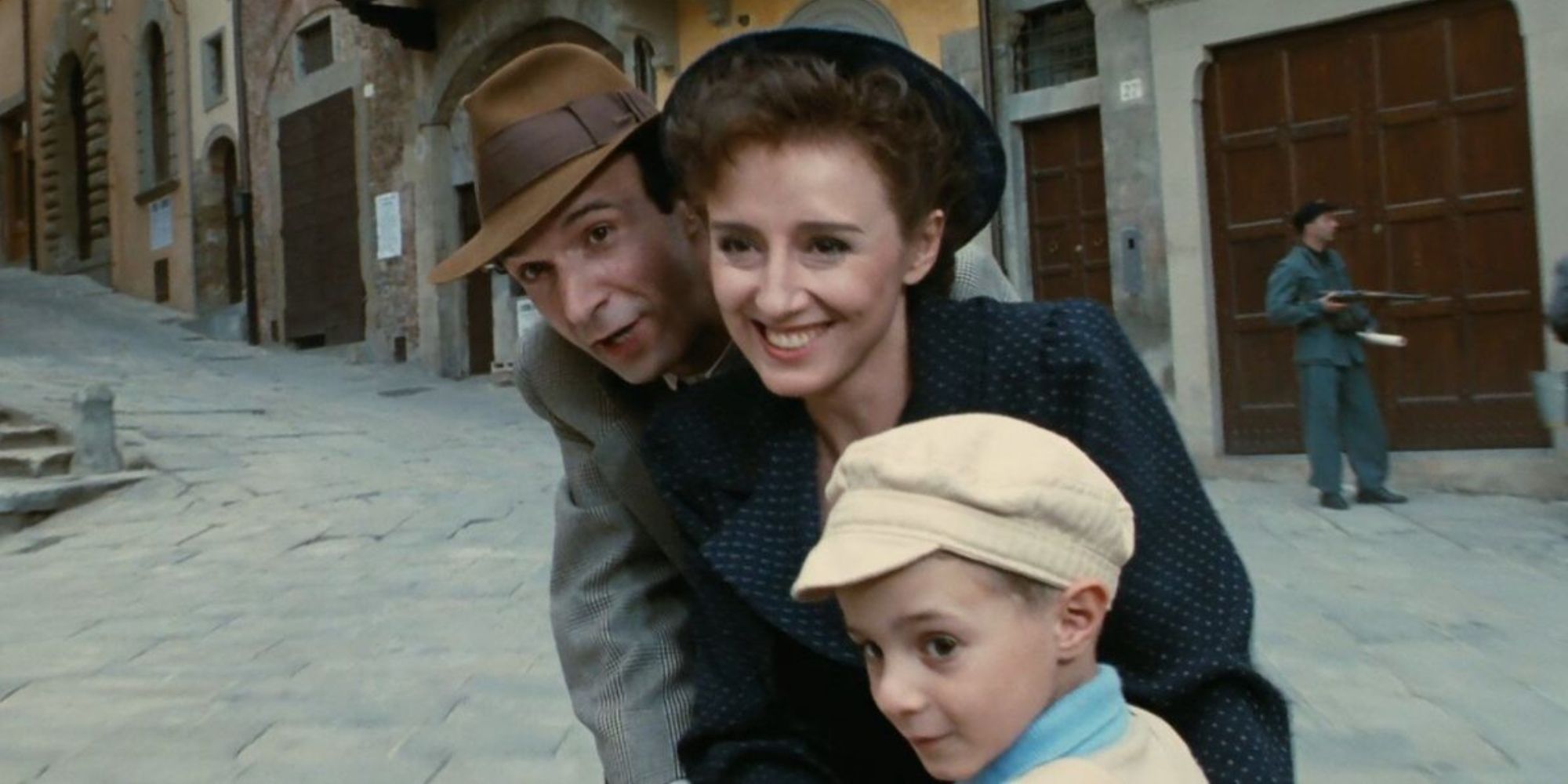 Guido, Dora, and Giosué riding a bike down a street in 'Life is Beautiful'