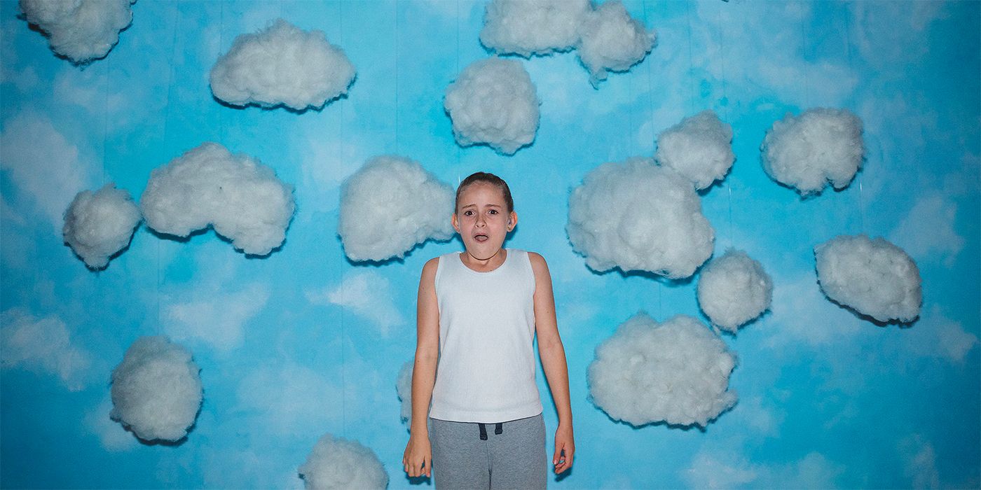 Lola Campbell standing in front of a blue wall with cotton clouds in the film Scrapper