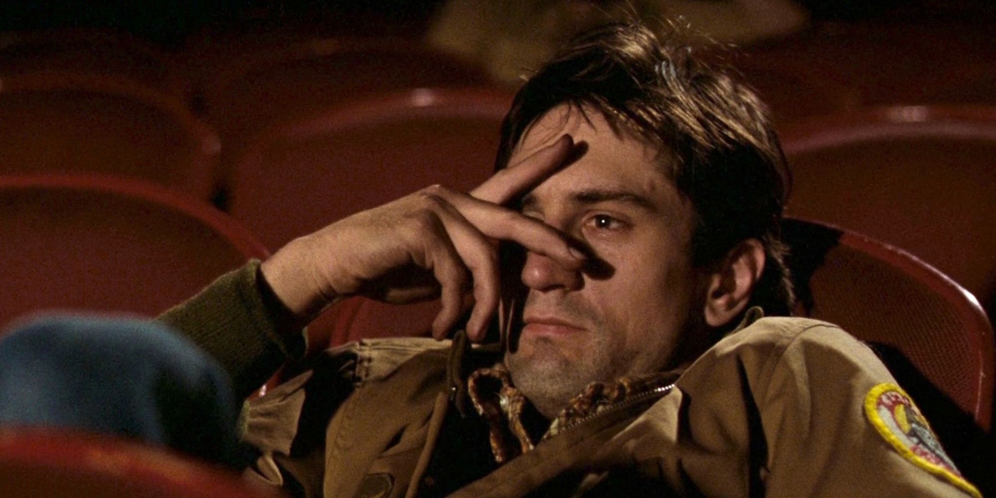 A close-up shot of Robert De Niro hiding his face behind two fingers while sitting in a movie theater in Taxi Driver.