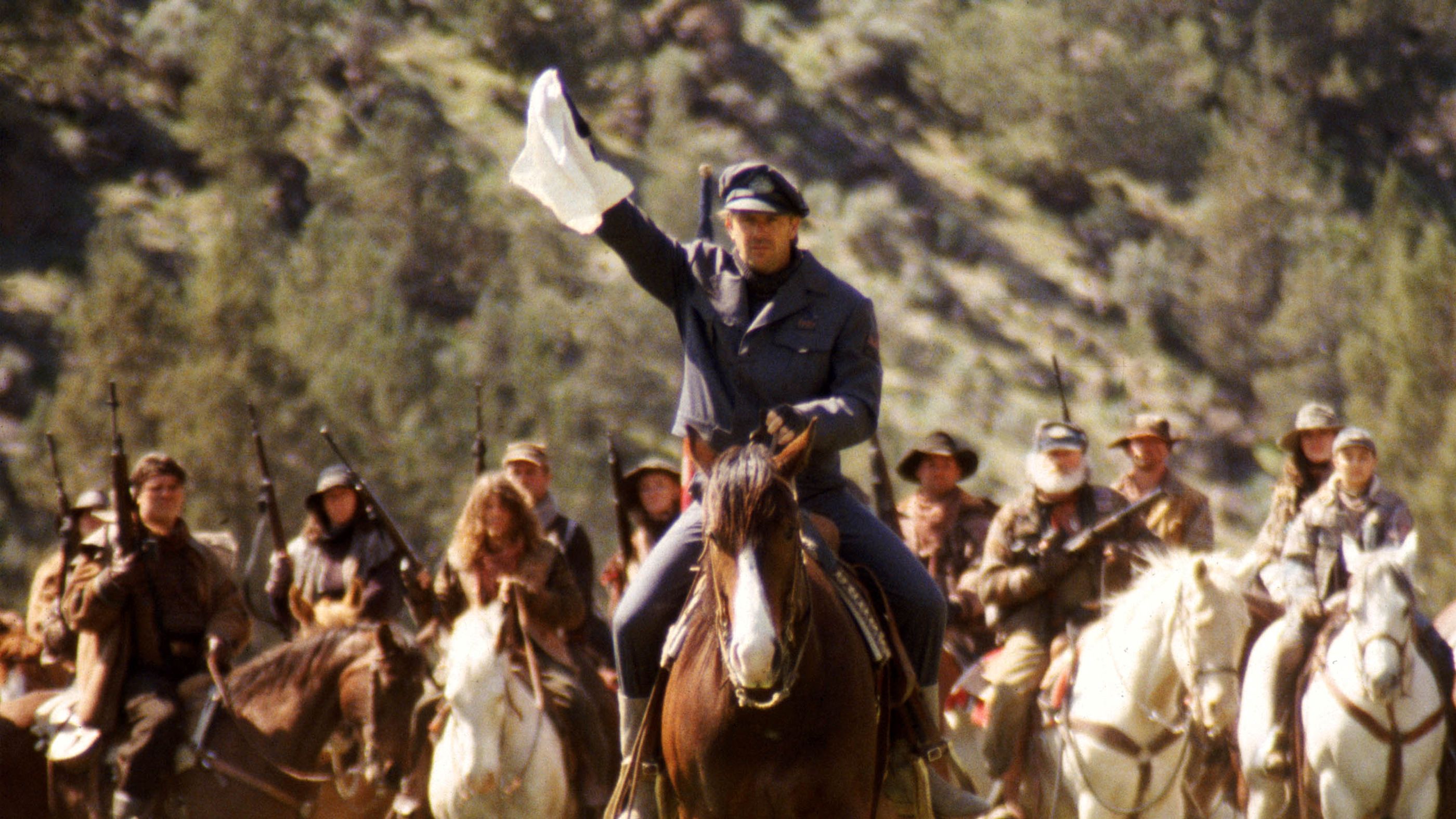 Kevin Costner on horseback holding a white flag in The Postman. 