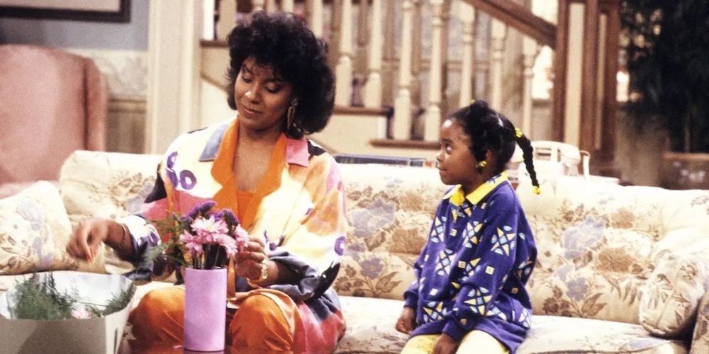 Phylicia Rashad dans le rôle de Clair Huxtable et Keshia Knight Pulliam dans le rôle de Rudy Huxtable, assises ensemble sur le canapé et arrangeant un vase de fleurs dans The Cosby Show.