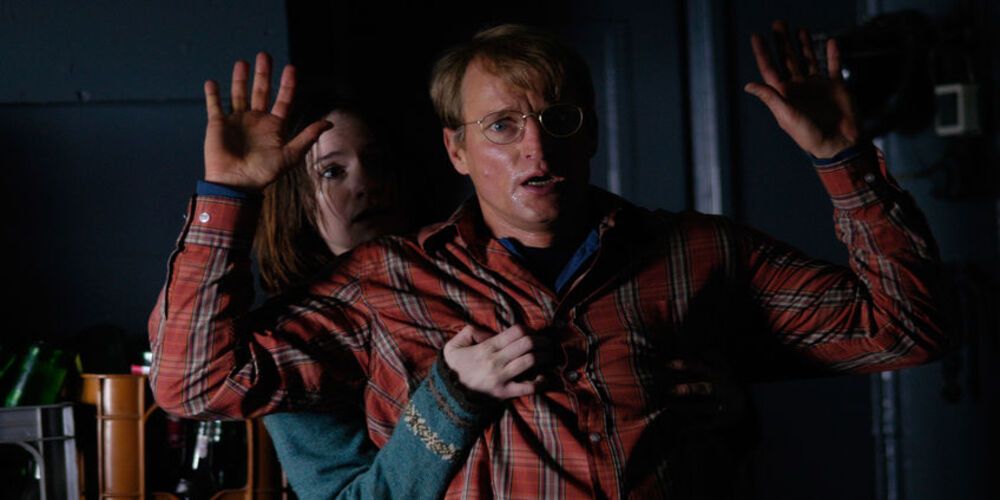 A screenshot of Woody Harrelson and Emily Mortimer in Transsiberian where he has his hands up and she is hiding behind him in fear