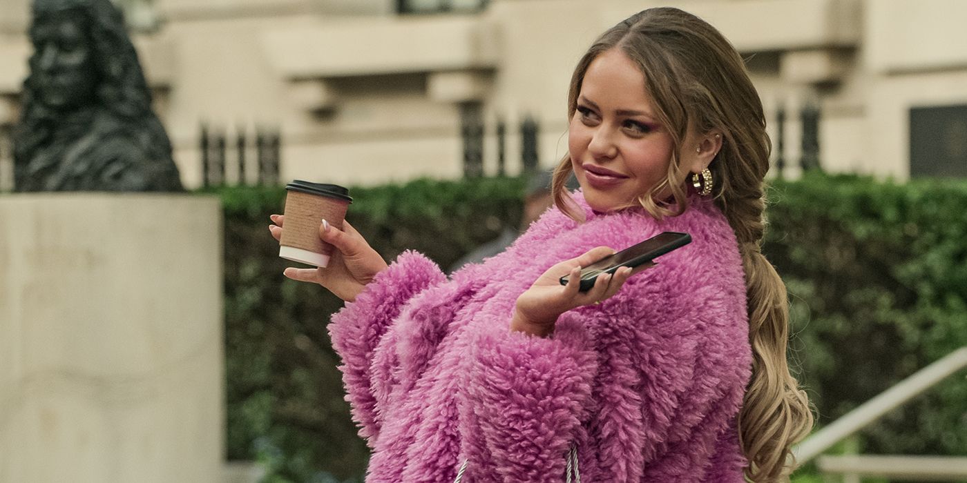 Gemma, jouée par Eve Austin, dans un manteau rose en fourrure, tenant une tasse de café dans une main et son téléphone dans l'autre, posant dans une scène de la saison 4 de You.