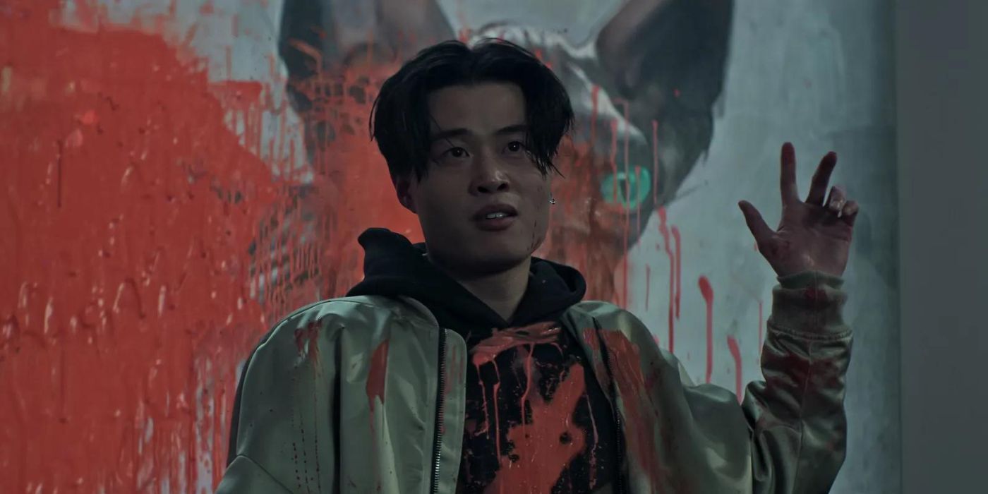 Simon yang diperankan oleh Aiden Cheng berdiri di depan reruntuhan lukisannya yang dilapisi cat merah di 'You' Season 4.