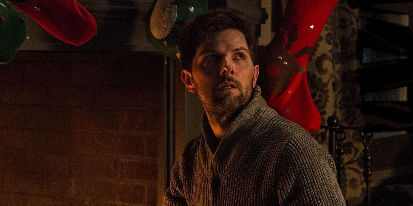Adam Scott looks fearful while kneeling by the hearth in Krampus