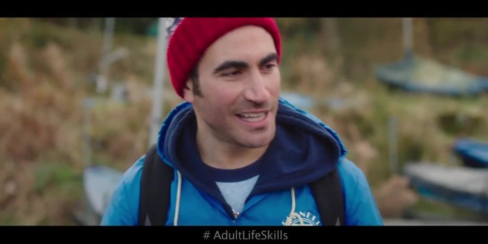 Capture d'écran officielle du film Adult Life Skills (2016) montrant Brett Goldstein fronçant les sourcils tout en parlant à quelqu'un, portant un sweat à capuche et une veste.