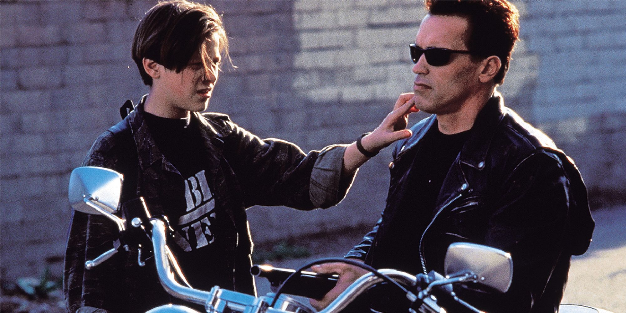 Edward Furlong dans le rôle de John Connor touche le visage de Terminator d'Arnold Schwarzenegger alors qu'il est assis sur une moto dans Terminator 2. 
