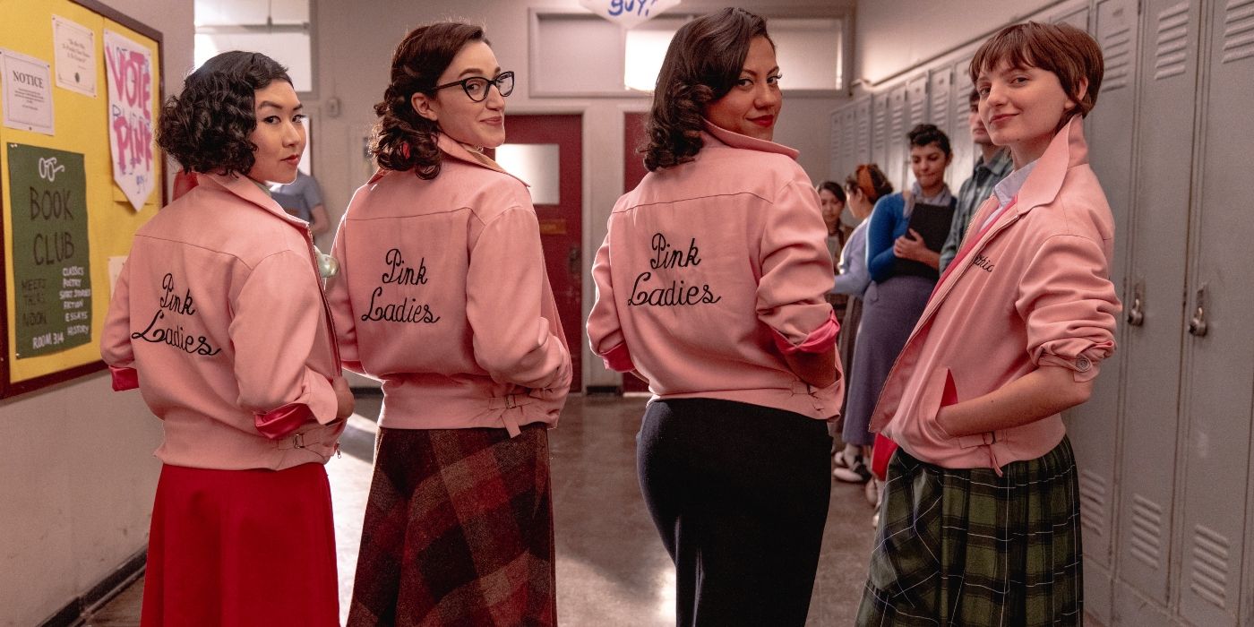 The cast of Grease: Rise of the Pink Ladies wearing their iconic pink jackets and turning to smile at the camera in Episode 2