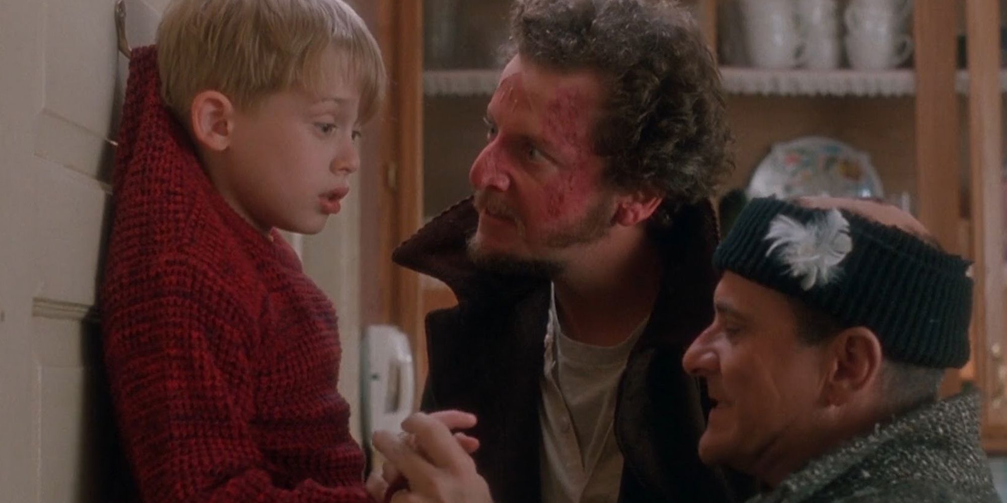 Kevin (Macaulay Culkin) hanging by a door hook while Harry (Joe Pesci) and Marv (Daniel Stern) look at him menacingly in Home Alone