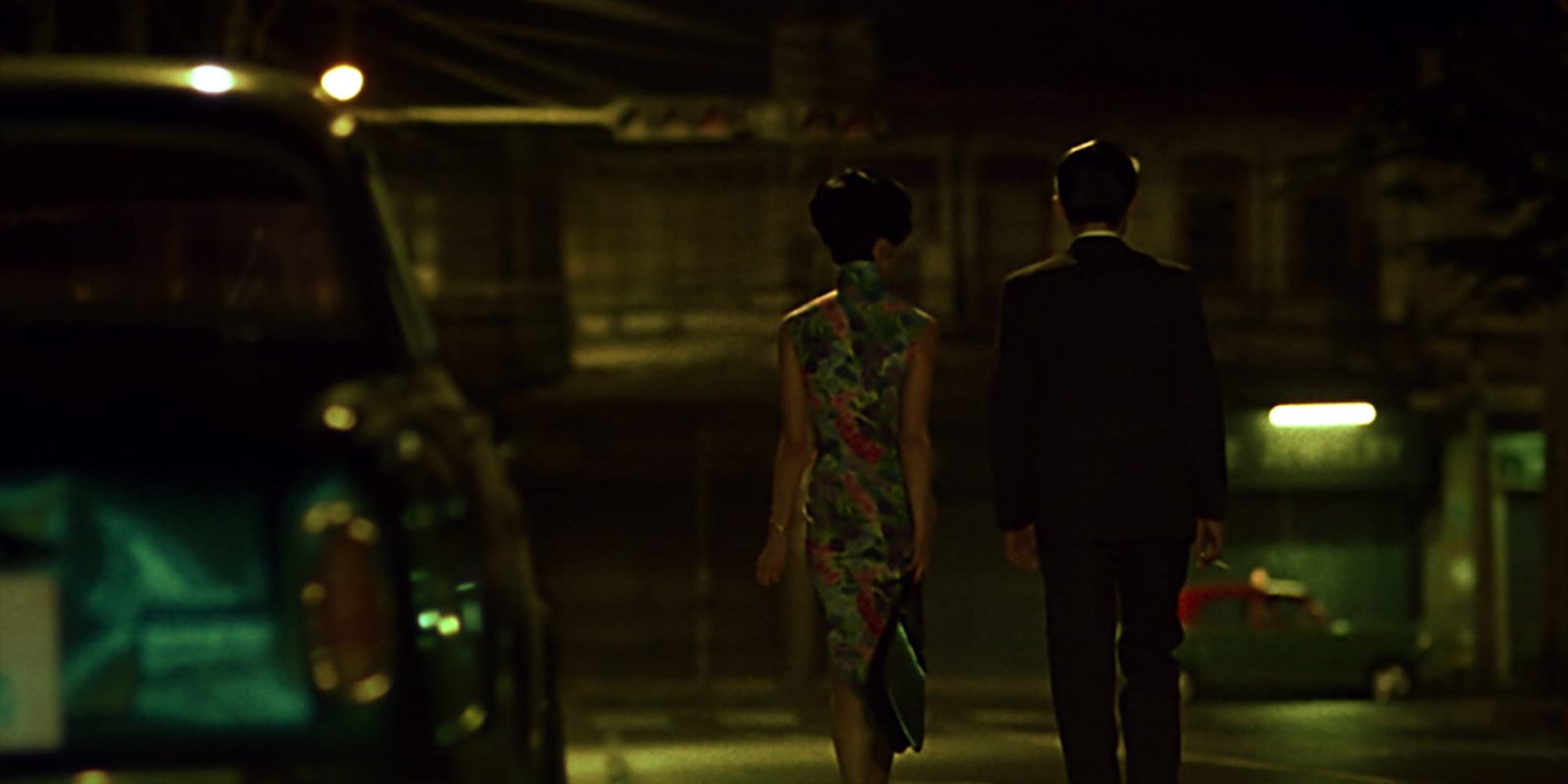 A man and woman walk through a dark city street in In The Mood For Love.