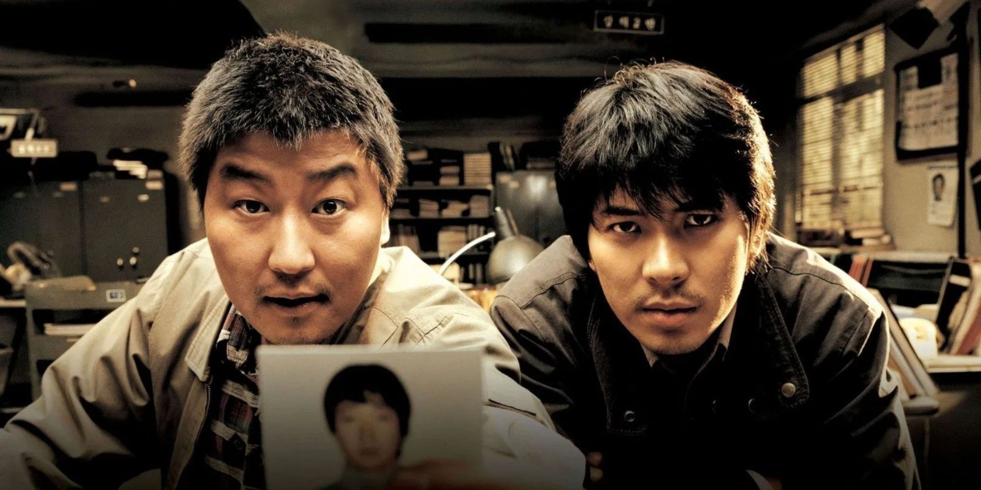 Two men facing the camera and holding up a man's polaroid in Memories of Murder