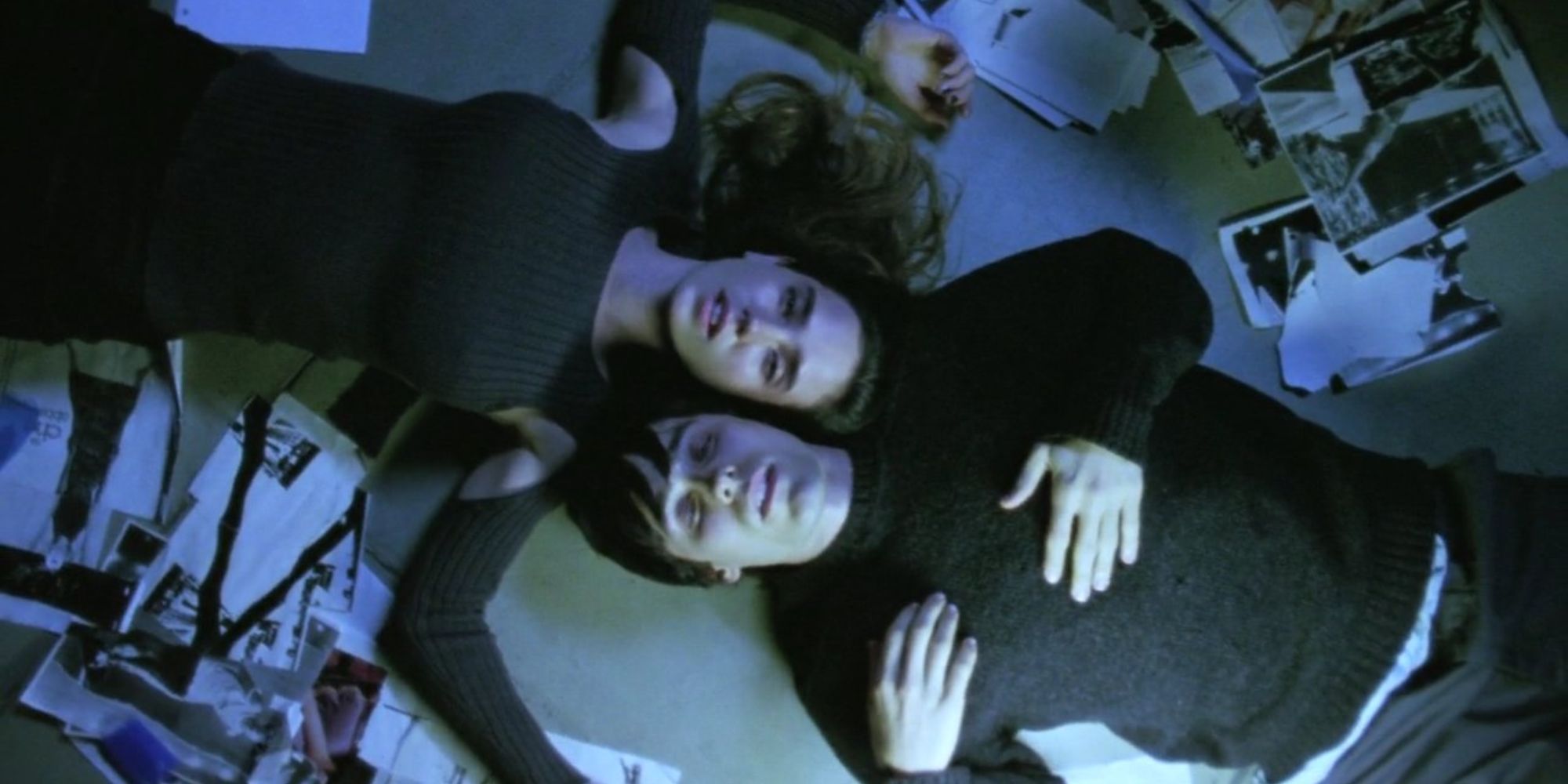 Two people lay on a floor with their heads next to each other and pages scattered around in Requiem For a Dream