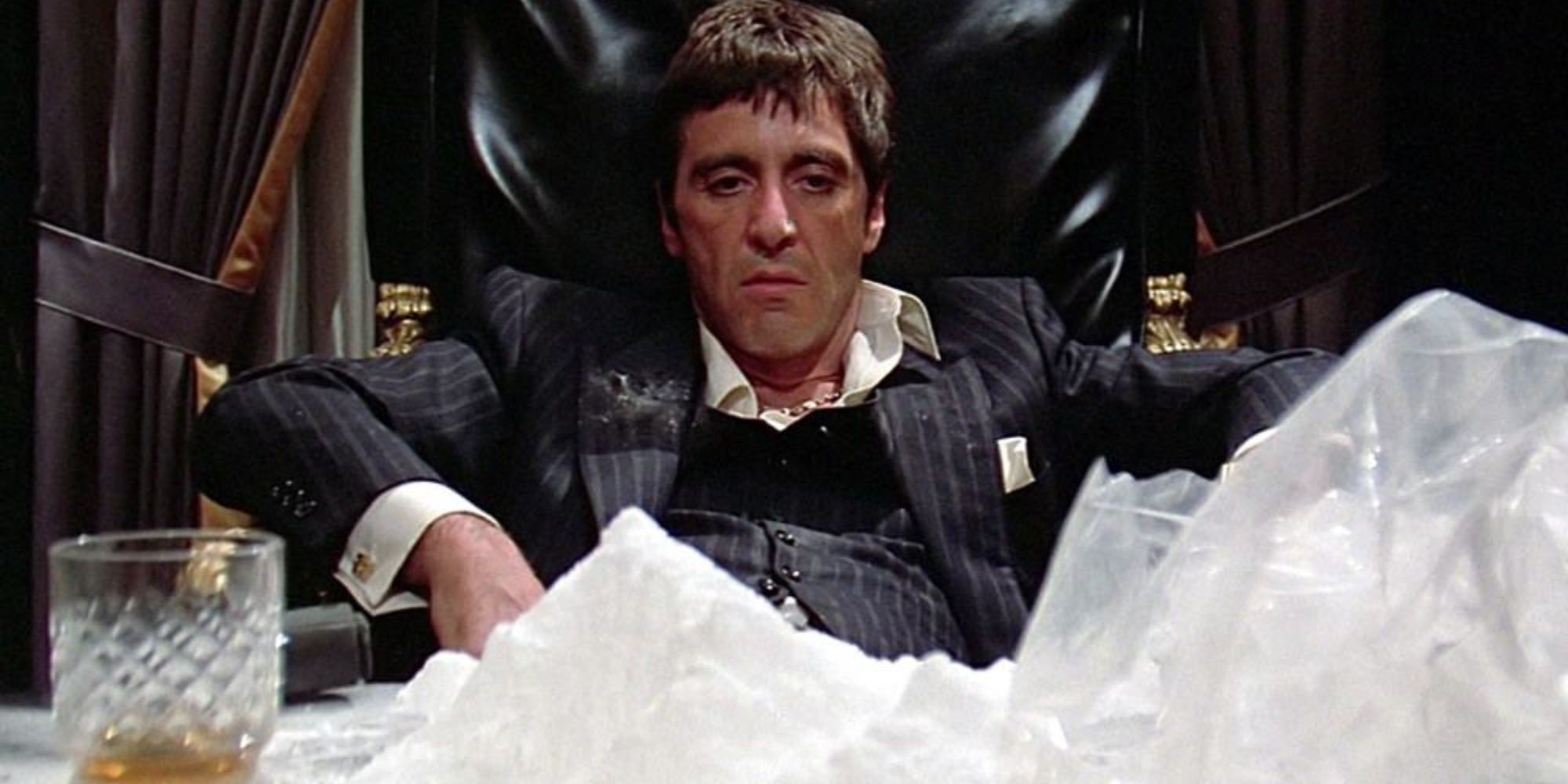 Tony Montana sitting down looking at his desk covered with bags of cocaine in Scarface (1983)