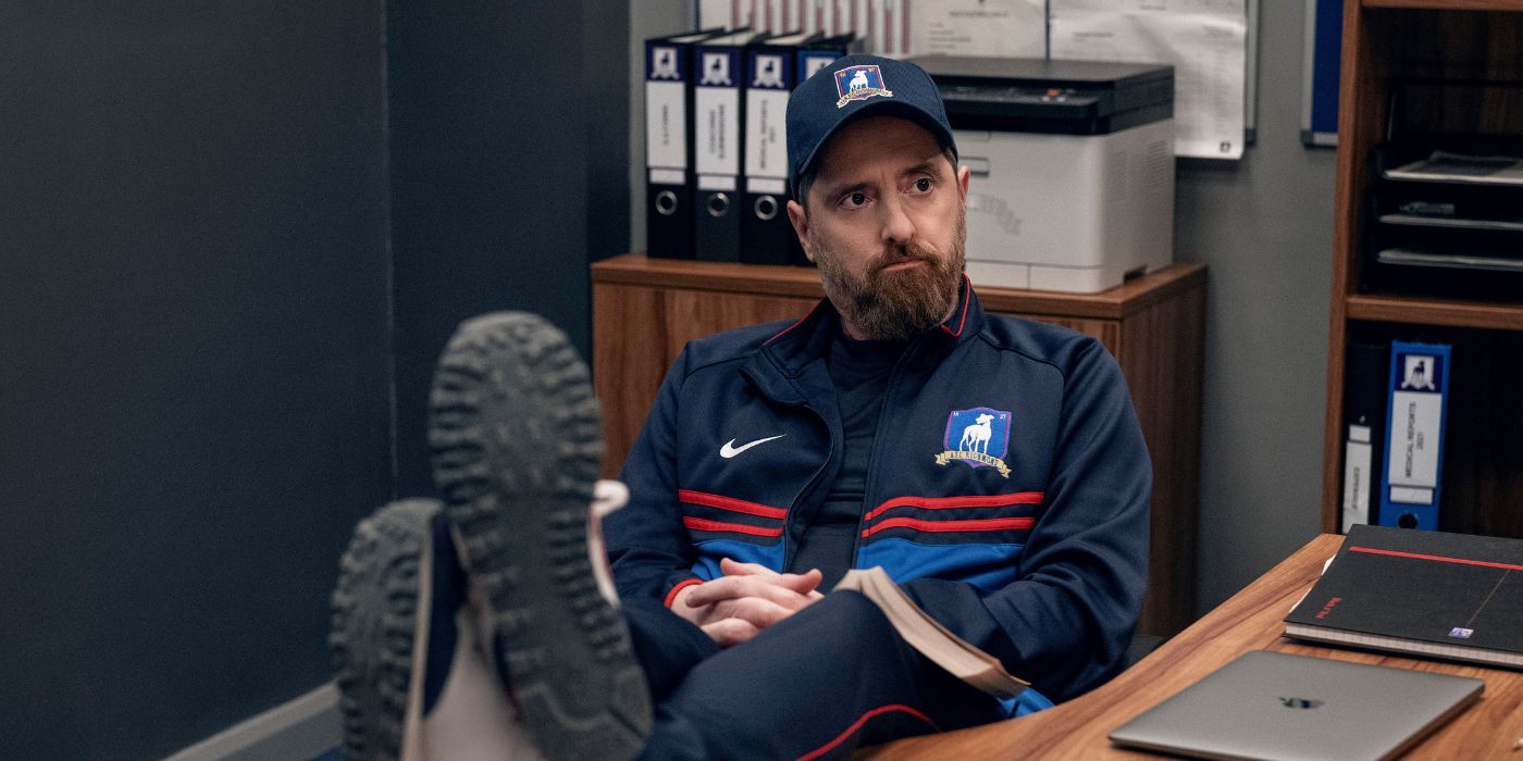 Brendan Hunt sits at the desk of Ted Lasso's season 3 coach Beard