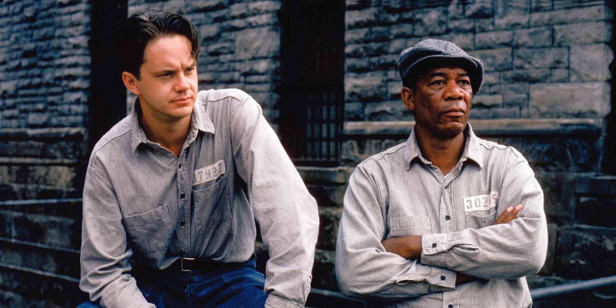 Tim Robbins and Morgan Freeman as Andy Dufresne and Ellis Boyd "Red" Redding, sitting in prison uniforms in The Shawshank Redemption