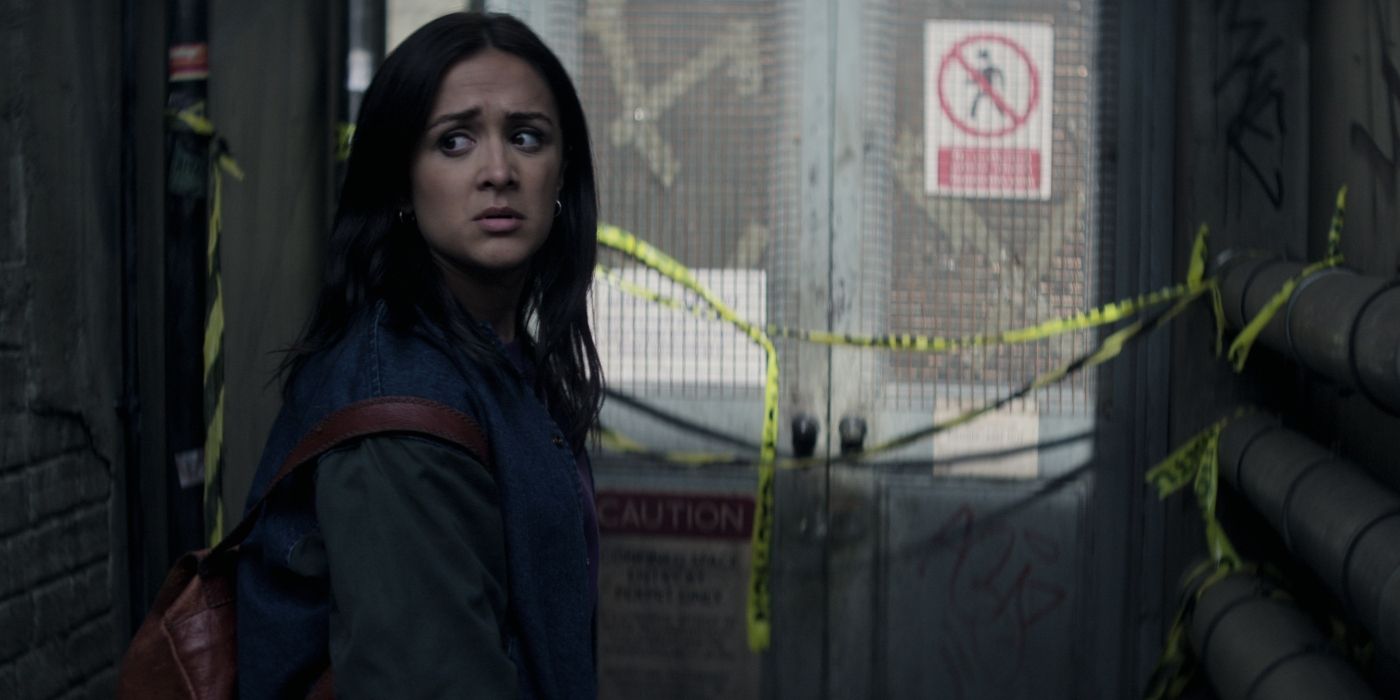 Nadia, played by Amy-Leigh Hickman, wearing a backpack and looking behind her in concern in front of a sealed off door in You Season 4