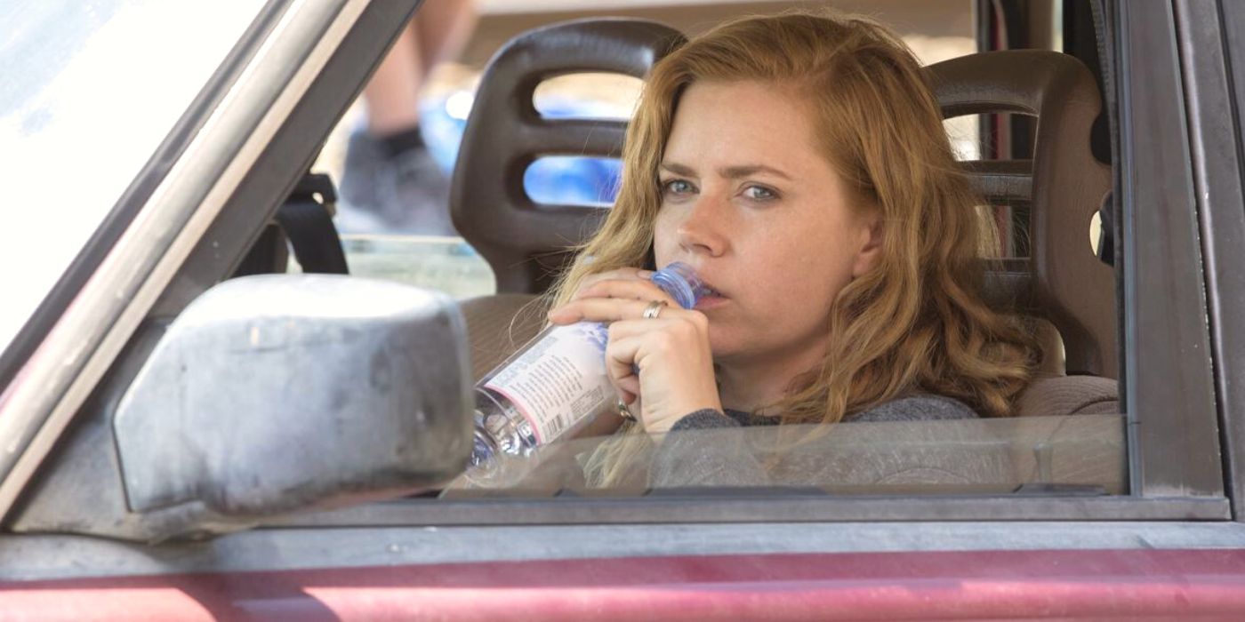 Amy Adams regarde sa voiture assise sur le siège du conducteur en train de boire dans une bouteille d'eau dans Sharp Objects