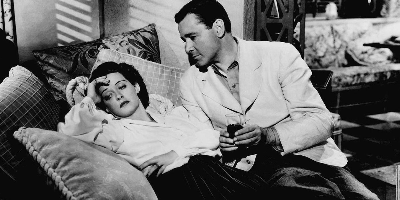Bette Davis lying on a couch looking forlorn with Herbert Marshall holding a drink nearby in The Letter.