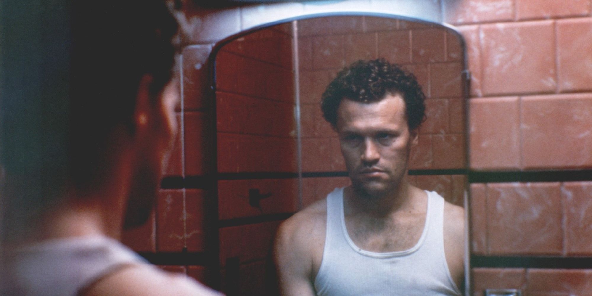 Henry, wearing a tank top, looks in the mirror moodily in Henry: Portrait of a Serial Killer