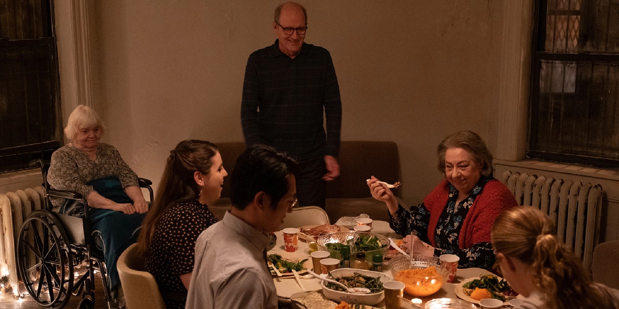 Erin Blake standing at the head of the table while his family looks at him in The Humans.