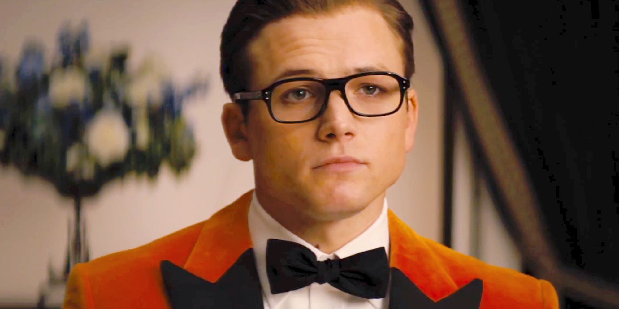 A closeup of Eggsy wearing an orange tuxedo and black framed glasses in Kingsman: The Golden Circle