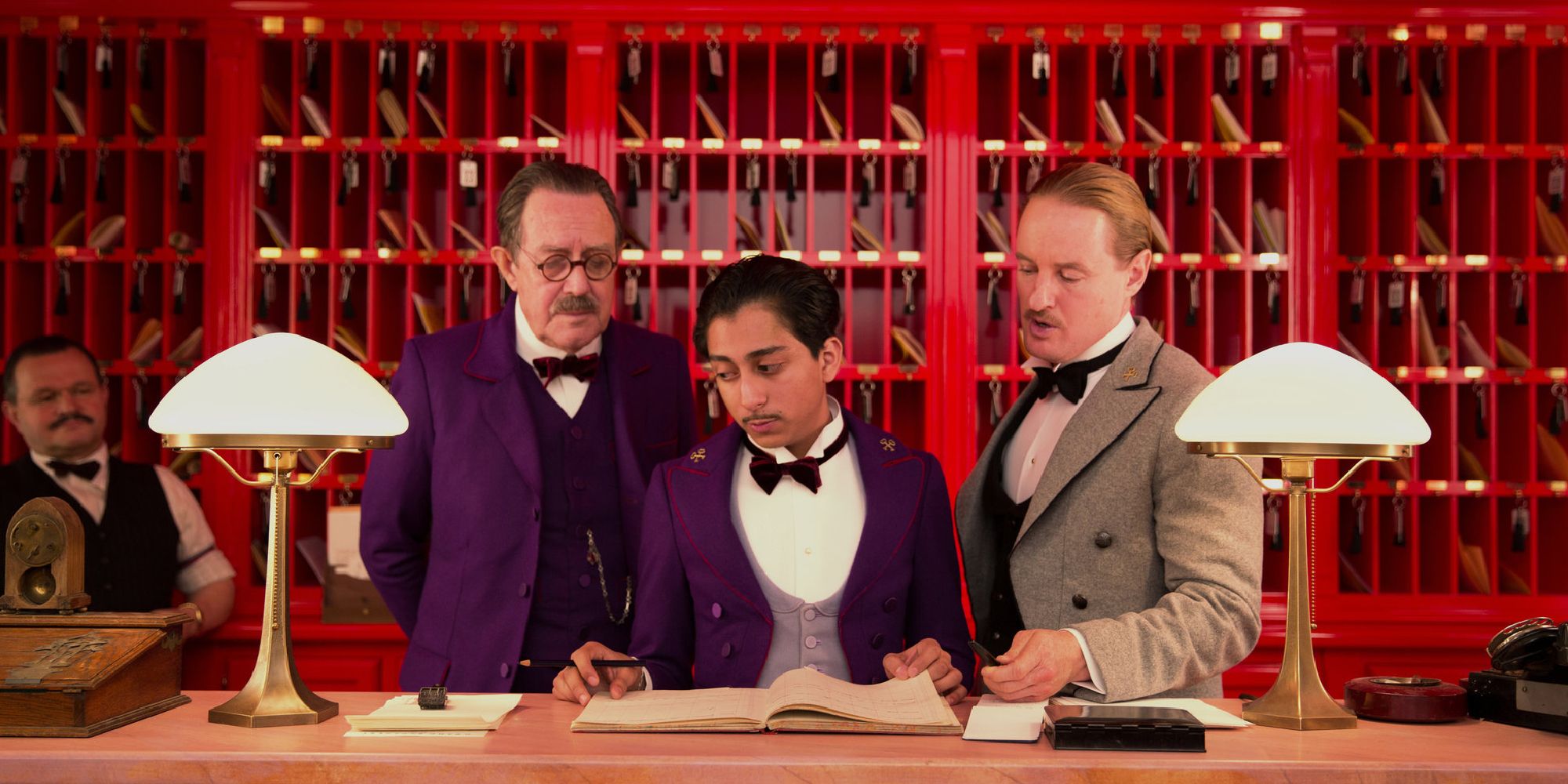 Owen Wilson and Tony Revolori look at a ledger at the lobby's front desk in The Grand Budapest Hotel