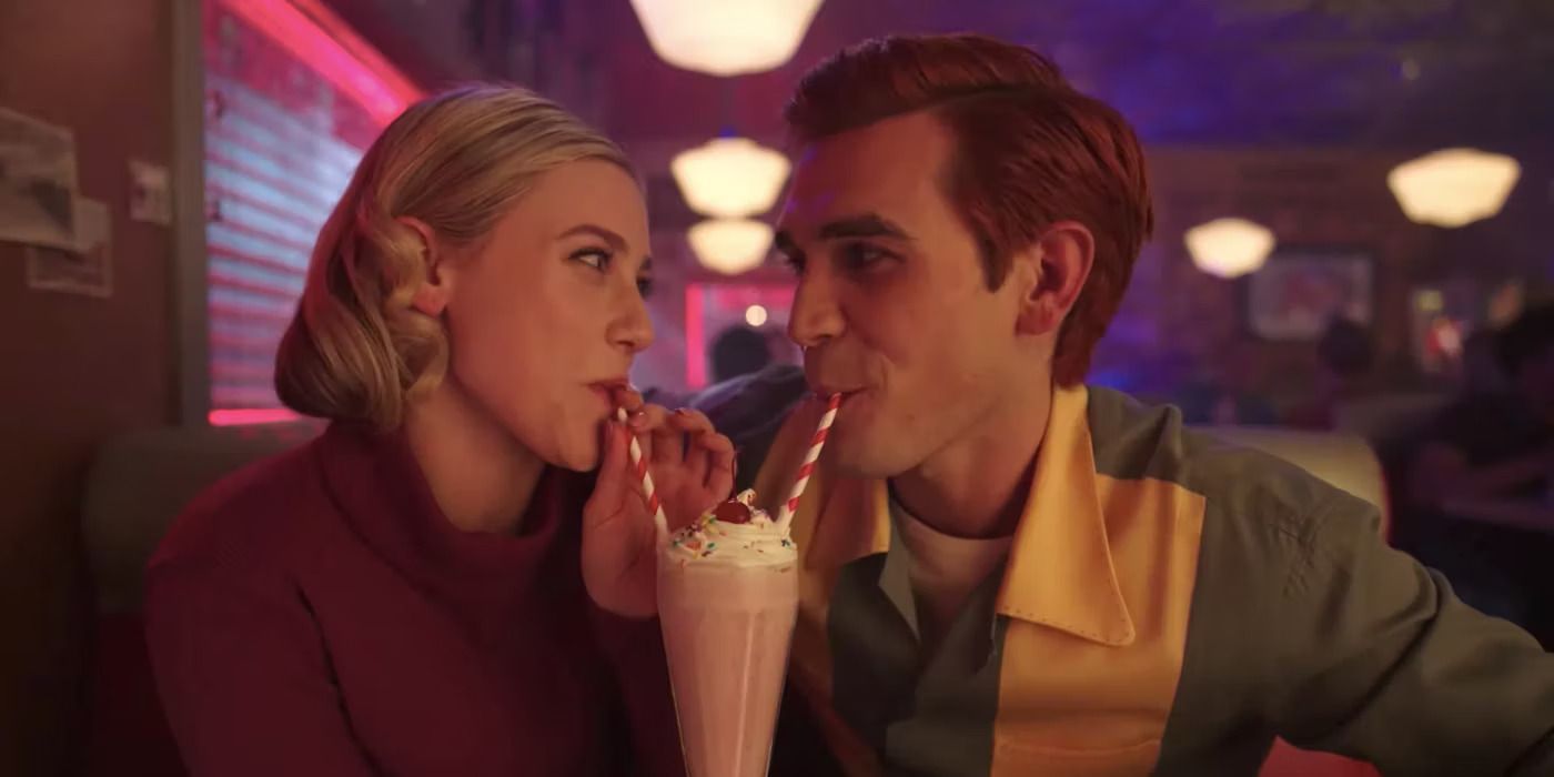 Betty (Lili Reinhart) and Archie (KJ Apa) smiling and drinking from the same milkshake with two straws in a diner in Riverdale Season 7
