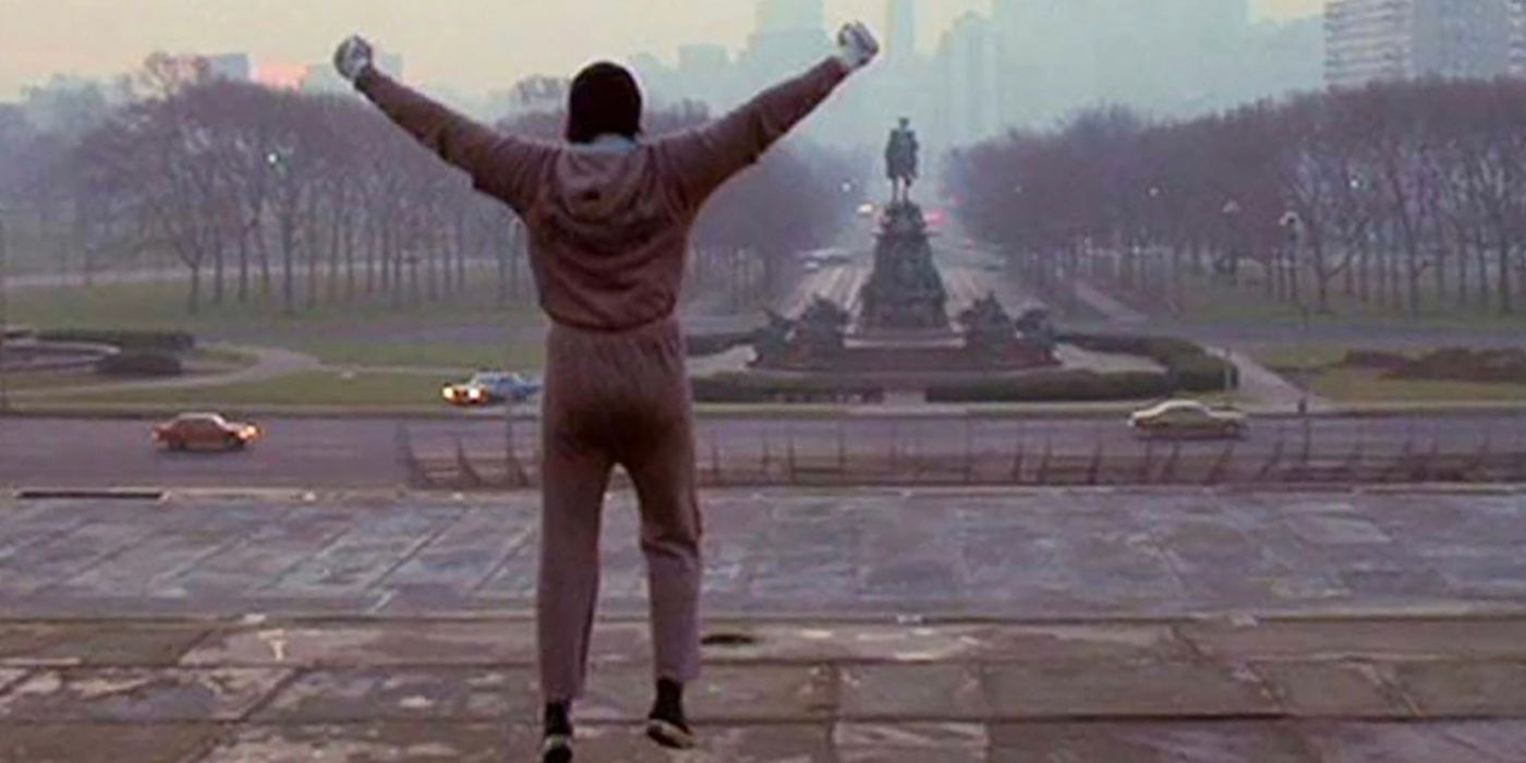 Rocky at the top of the stairs from Rocky III, jumping up hands in the air.