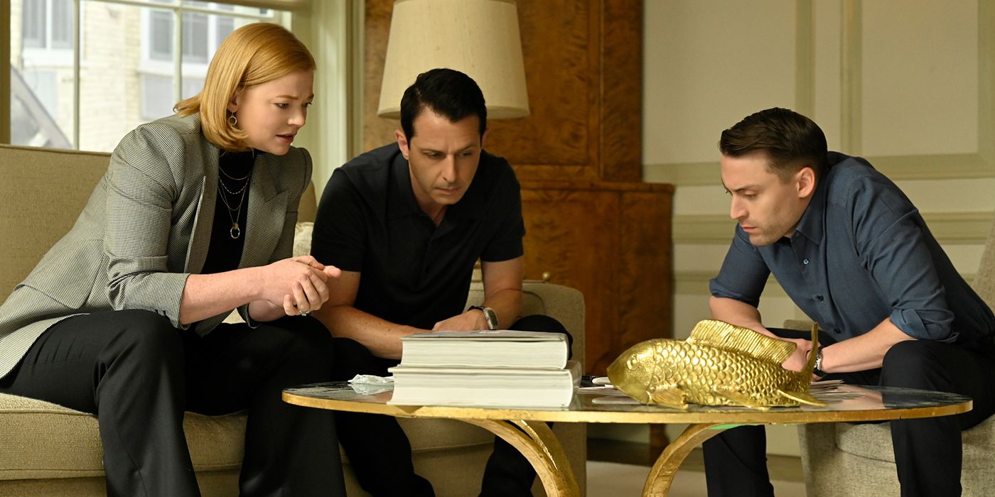 Shiv, Kendall, and Roman sitting around a table looking at something in a scene from Succession.