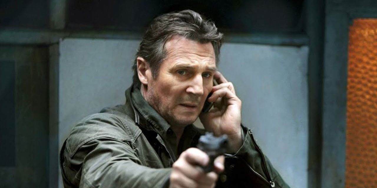 Liam Neeson on the phone as he aims a gun in Taken