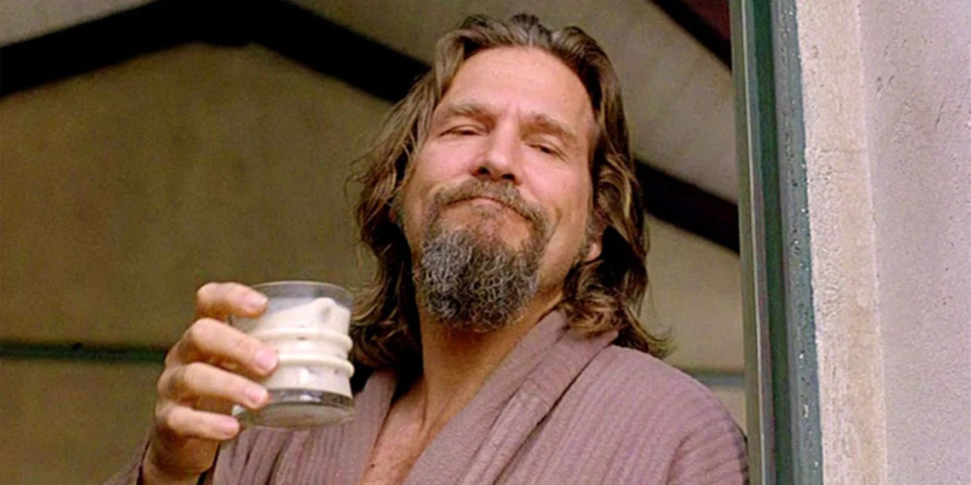 Jeffrey "the Dude" Lebowski (Jeff Bridges) stands in his doorway wearing a dressing gown and flaunting a glass of milk.