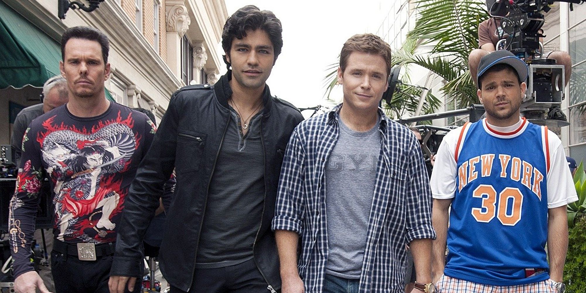 The crew of &lsquo;Entourage&rsquo; walking with swagger toward the camera with a film set with palm trees in the background.