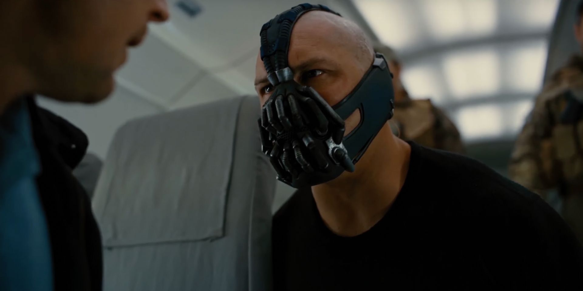 A masked mercenary glares into the eyes of a CIA agent on a plane. 